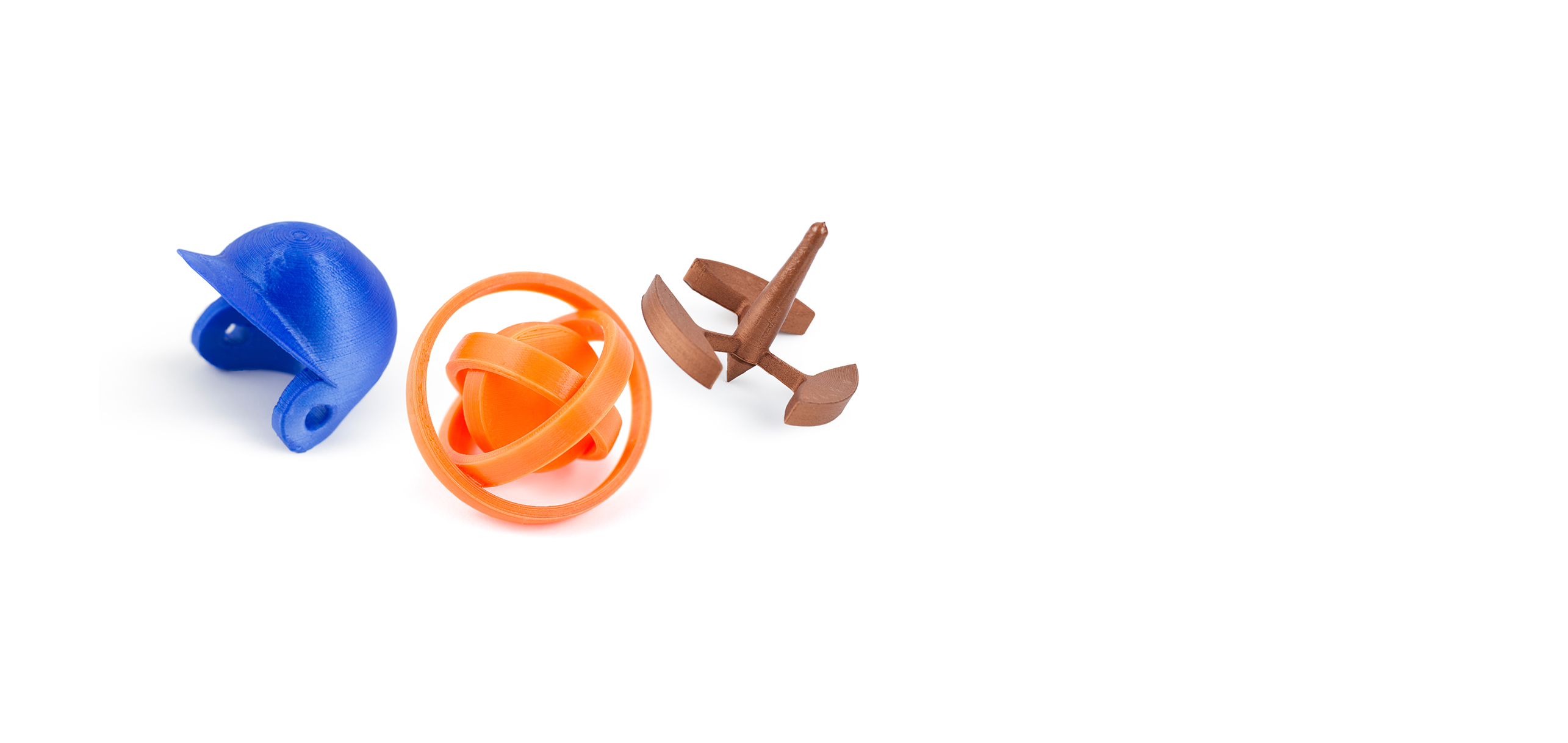 Three colorful 3D-printed objects on a white background: a blue object resembling a helmet or shell, an orange spherical object with intersecting rings, and a brown object resembling a small propeller or anchor.