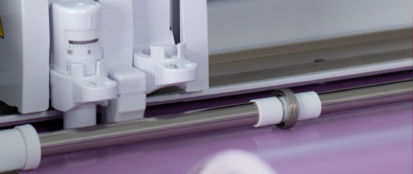 Close-up view of a cutting machine's blade and roller mechanism with a purple material being loaded.