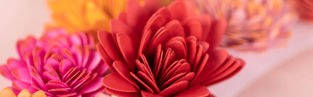 Close-up image of colorful paper flowers in red, pink, and yellow hues, showcasing detailed petal designs.